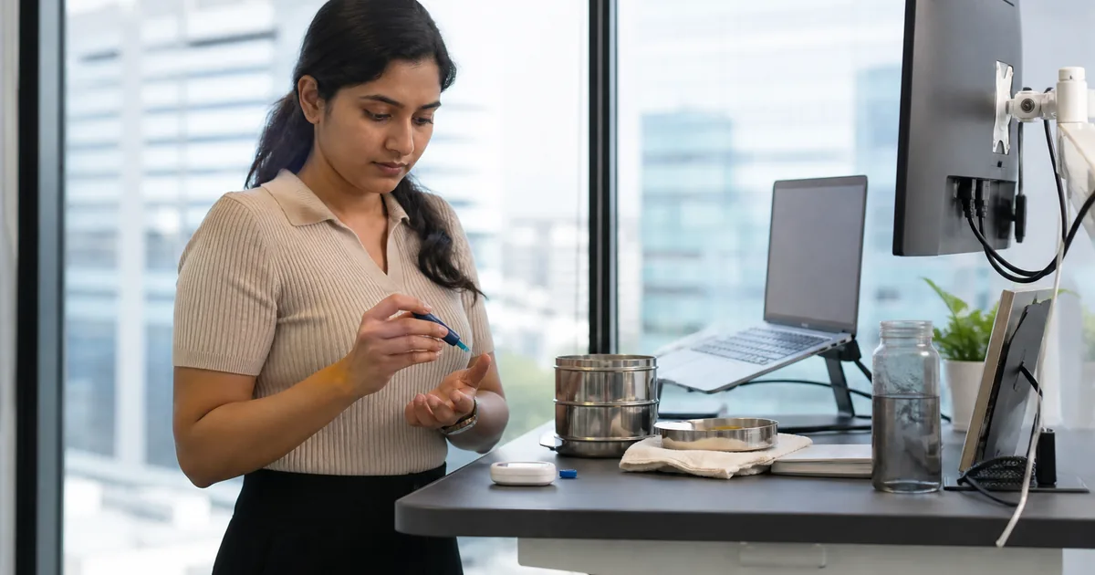Young Indian office worker with a home glucose meter and tiffin at a desk