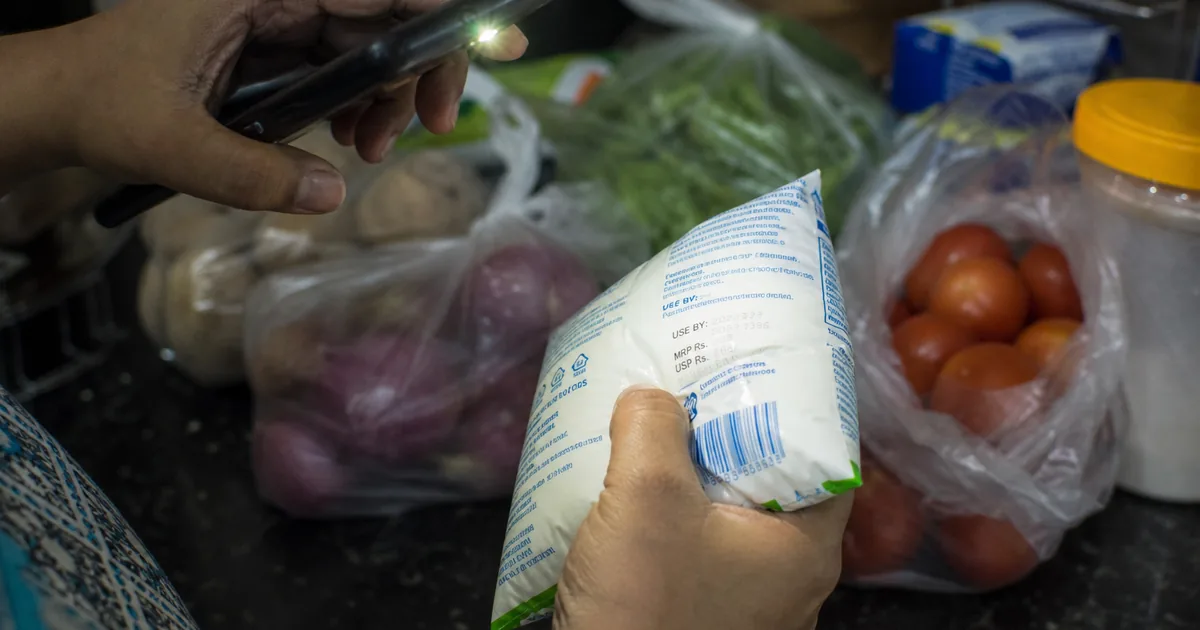 Hands checking a use-by date on a milk packet with a phone light